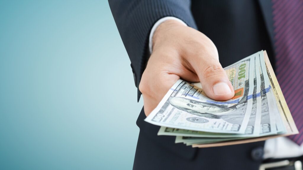 Man in suit giving money, representing the FTC refund payments for May.