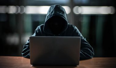 A hooded hacker behind a laptop, representing the Schneck Medical Center data breach settlement.