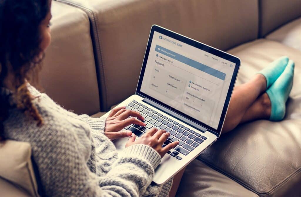 A woman sits on a sofa with her legs stretched out as she works on a laptop, representing the class action settlements closing soon.