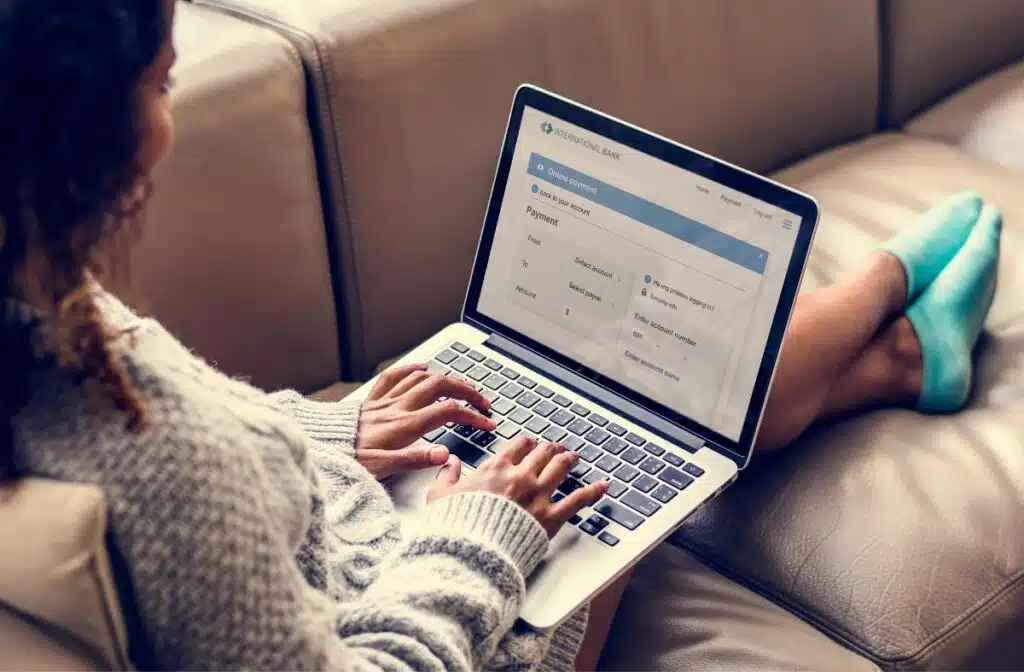 A woman sits on a sofa with her legs stretched out as she works on a laptop, representing the class action settlements closing soon.
