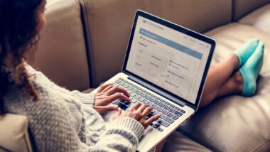 A woman sits on a sofa with her legs stretched out as she works on a laptop, representing the class action settlements closing soon.