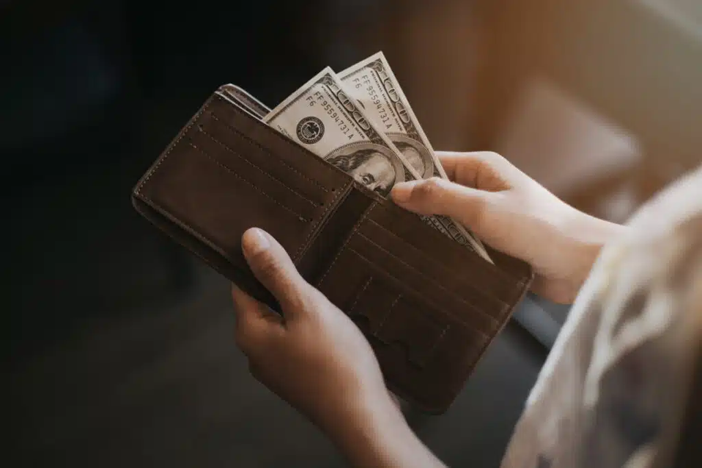 Close up of hands pulling cash out of a wallet, representing recent class action rebates.