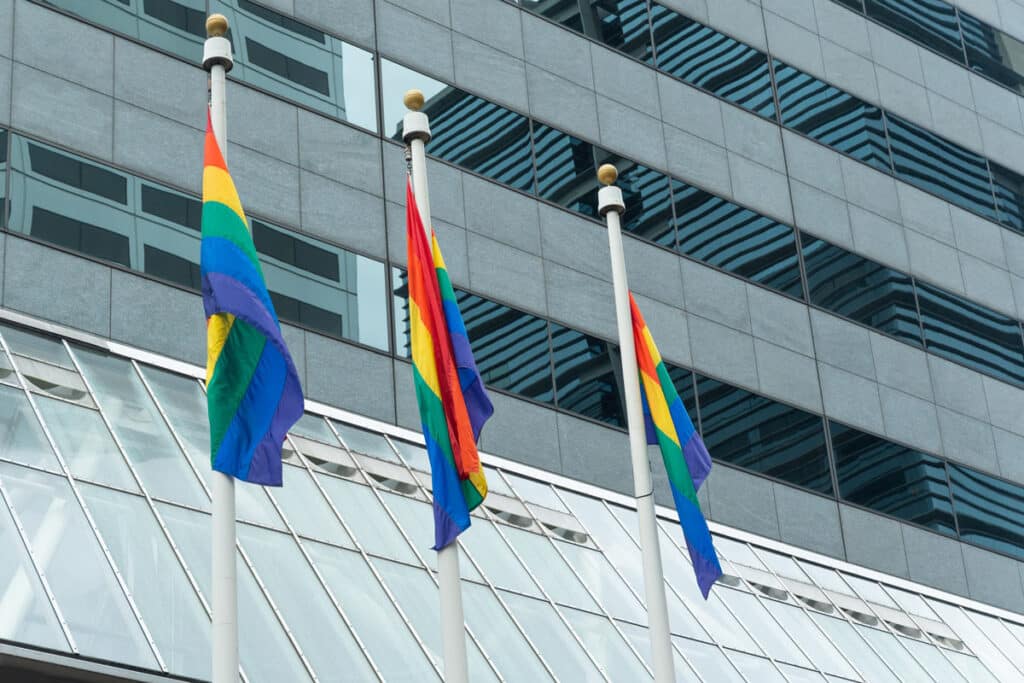 Three pride flags hang on a pole, representing the same-sex weddings web designer lawsuit.