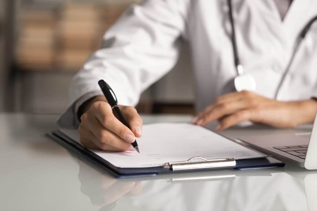 Close up of a doctor filling out paperwork, representing the Geico lawsuit.