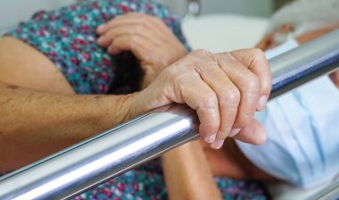 Close up of an elderly woman's hands holding a bed rail, representing adult bed rails.