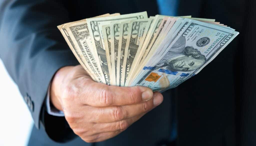 Suited man handing over cash money, representing recent FTC refunds.