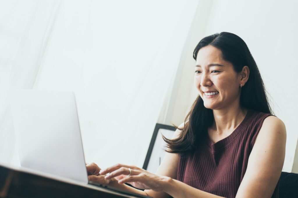 A smiling woman sits in a white room, using a laptop, representing the September settlement deadlines.