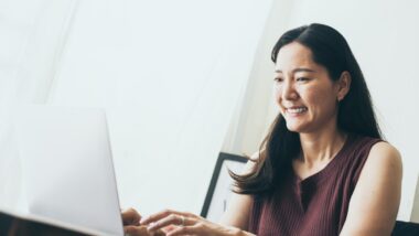 A smiling woman sits in a white room, using a laptop, representing the September settlement deadlines.