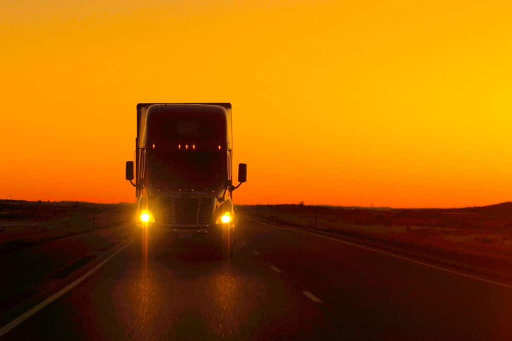 A semi truck driving along a ride against a bright sunset sky, representing the Yellow bankruptcy.