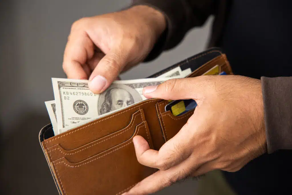 Close up of a mans hands pulling cash out of a wallet, representing recent class action rebates.