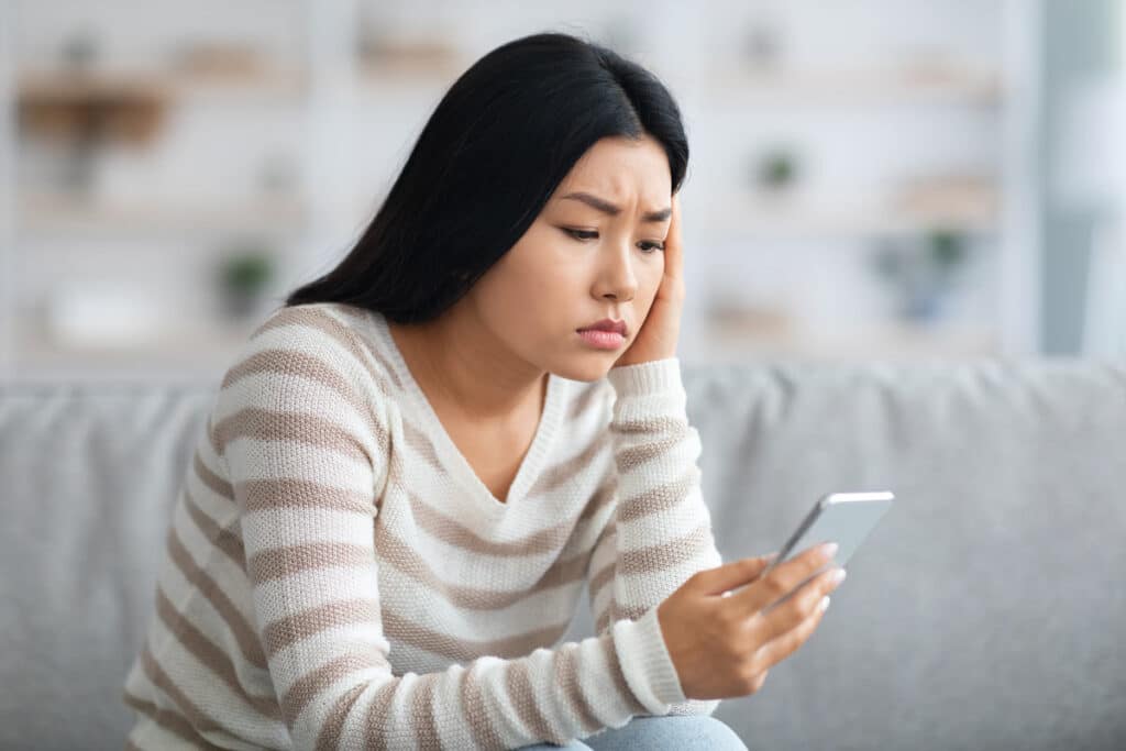 A frustrated woman looking at her phone, representing the Journeys texts class action lawsuit settlement.