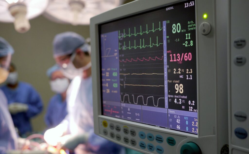heart surgery underway, moniter in the foreground surgeons and patient in background.