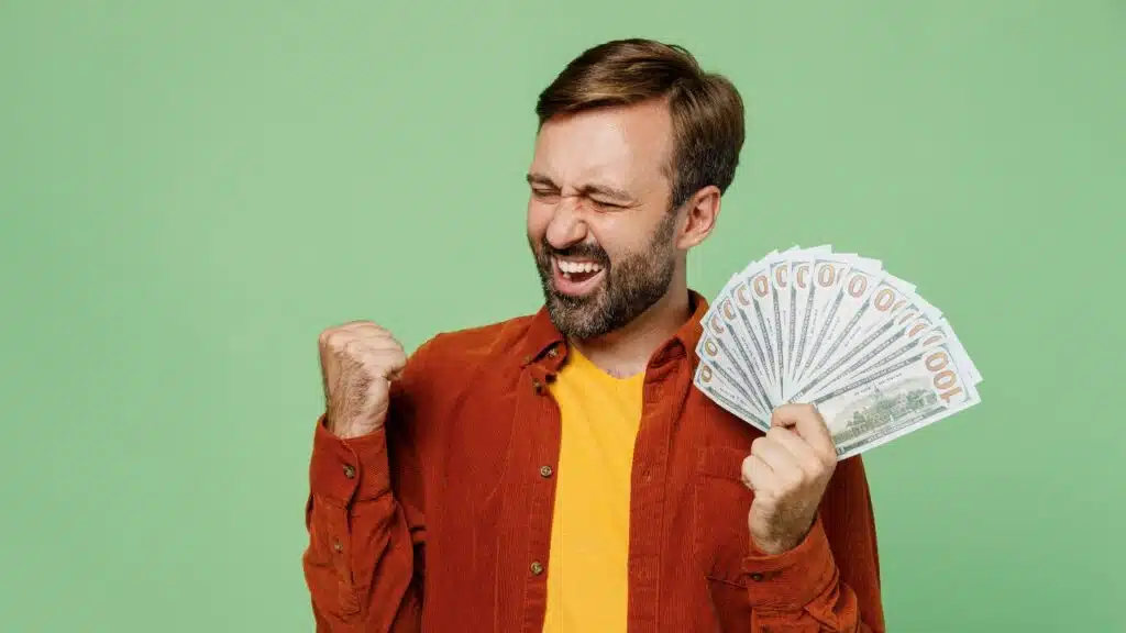 man with a fan of money in hand fist pumping in excitement.