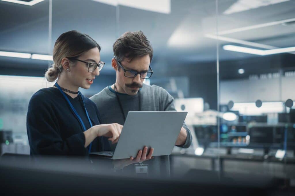 Two computer engineers working on a laptop, representing the White House AI development competition.