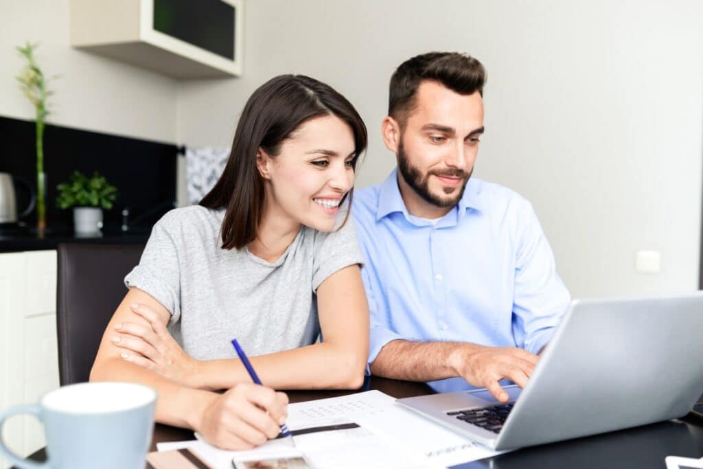 A man and woman sit at a table, looking at an open laptop, representing the class action settlement deadlines coming up in October.