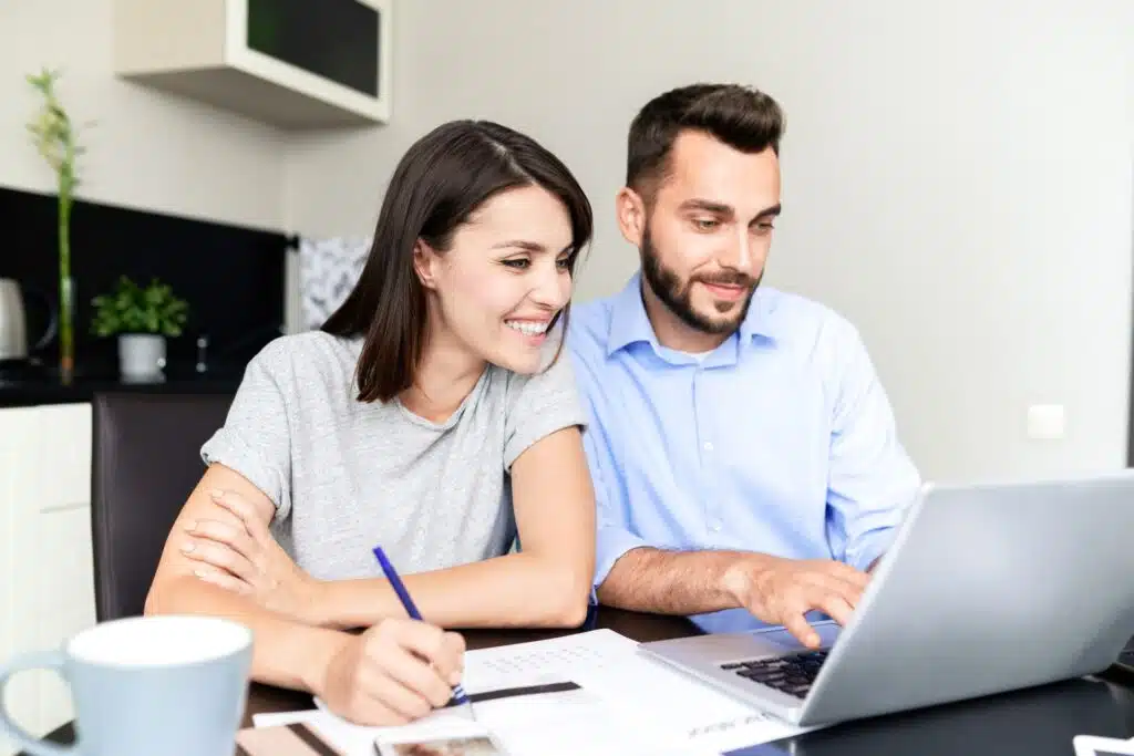 A man and woman sit at a table, looking at an open laptop, representing the class action settlement deadlines coming up in October.
