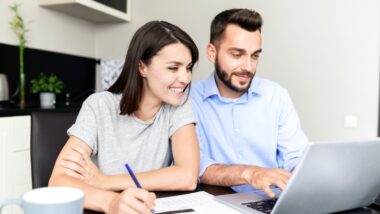 A man and woman sit at a table, looking at an open laptop, representing the class action settlement deadlines coming up in October.