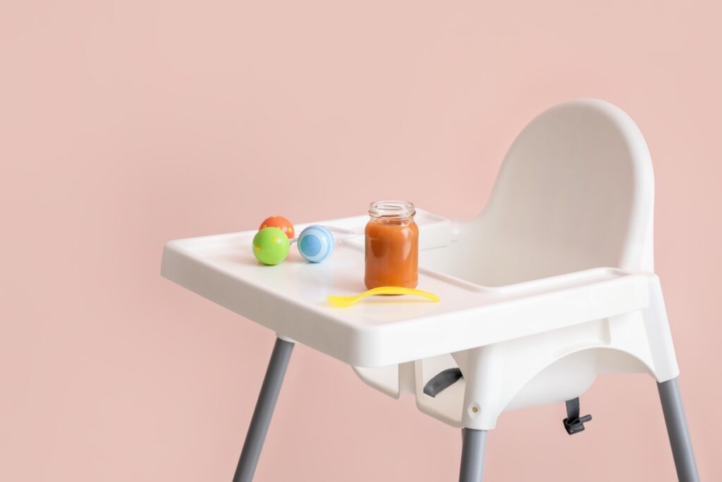 Baby highchair with food on color background