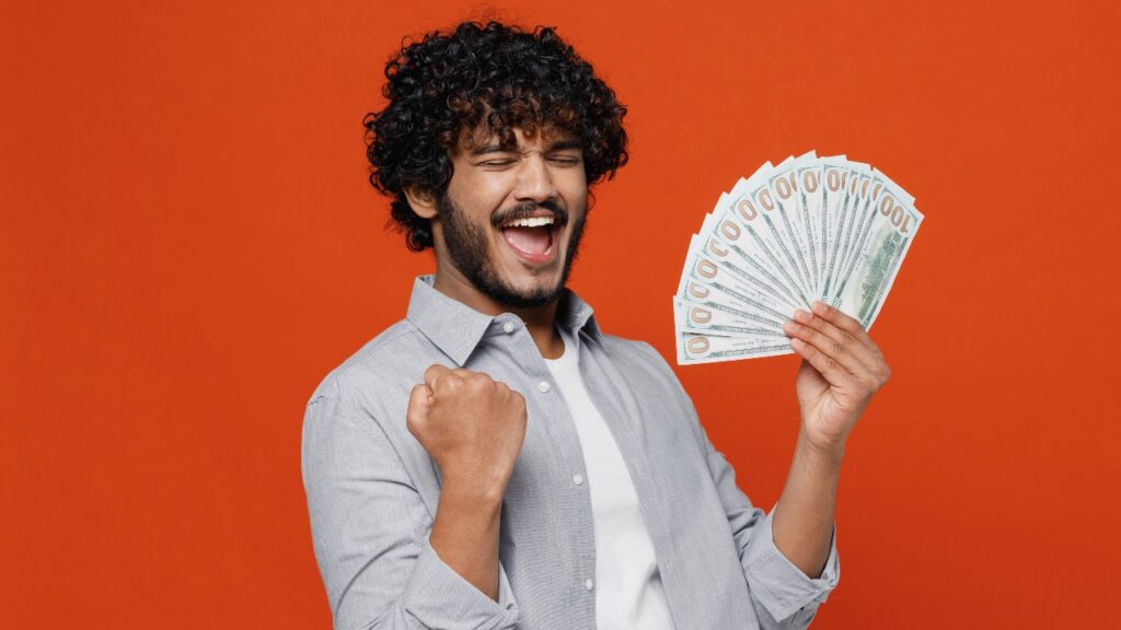 man 20s years old wears blue shirt holding fan of cash money in dollar banknotes doing winner gesture celebrate clenching fists