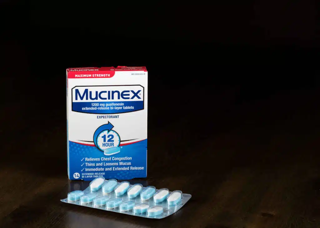 Mucinex extended release expectorant tablets and packet on wooden table representing the Mucinex and Alka Seltzer class action.