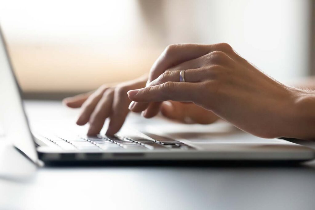 Close up of a womans hands typing on a laptop, representing the Immediate data breach settlement.