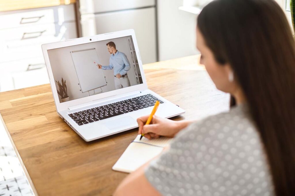 A female student taking notes while participating in online education, representing the Point Park University settlement.