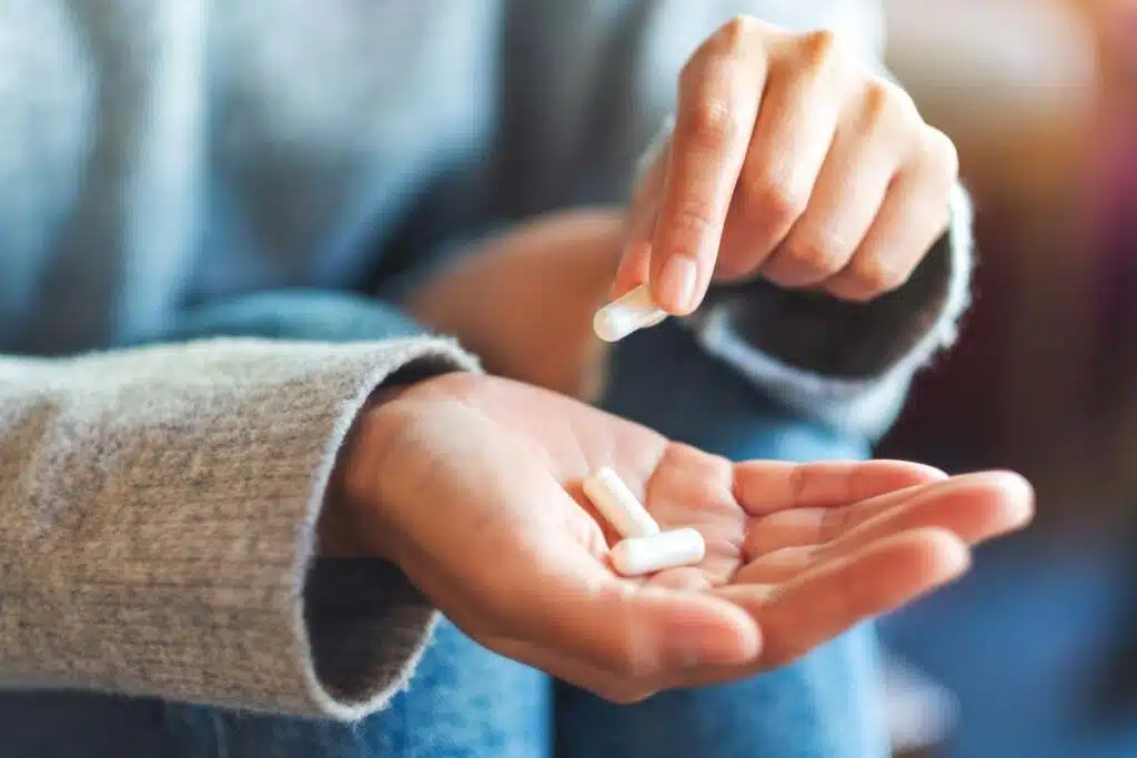 Close up of a woman's hand holding white capsules, representing the Botanical-Be supplements recall.
