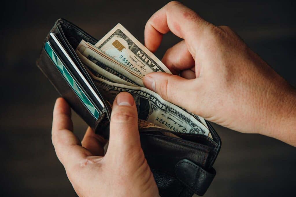 Close up of a mans hands putting cash into a wallet, representing FTC refund payments from August and September.