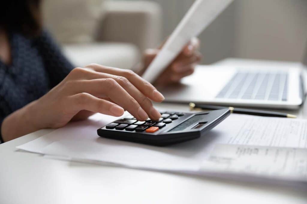 Close up of a woman's hand using a calculator to calculate a bill, representing the ACH litigation settlement.