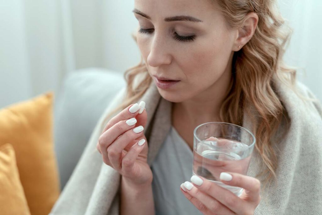 Close up of an ill woman holding a pill and glass of water, representing the class action lawsuits over allegedly ineffective phenylephrine.
