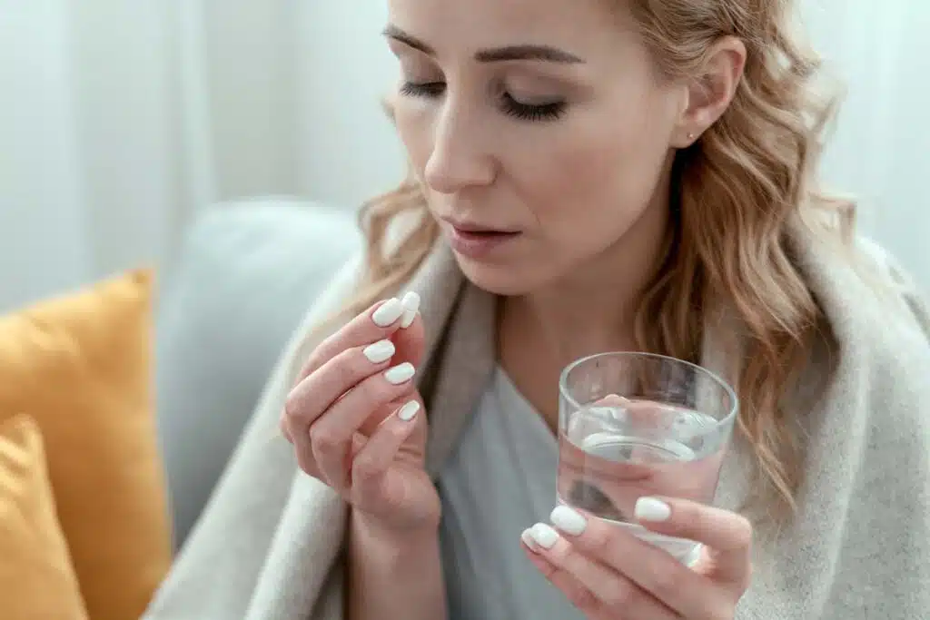 Close up of an ill woman holding a pill and glass of water, representing the class action lawsuits over allegedly ineffective phenylephrine.
