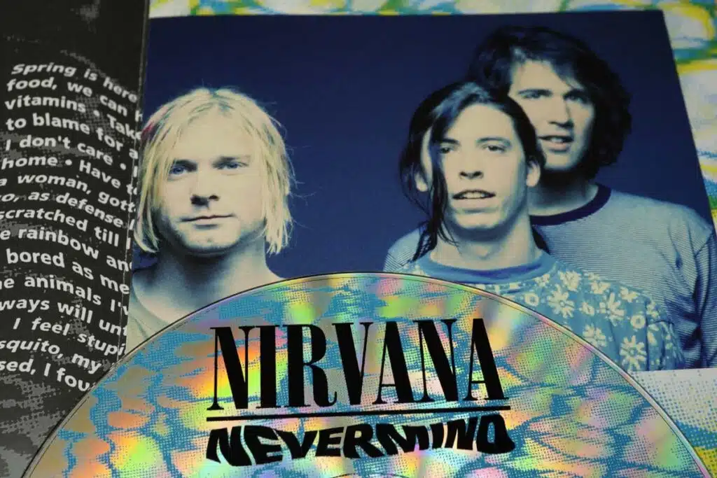 Nirvana Nevermind album CD atop a photo of Nirvana band members, representing the Nirvana baby child pornography lawsuit.