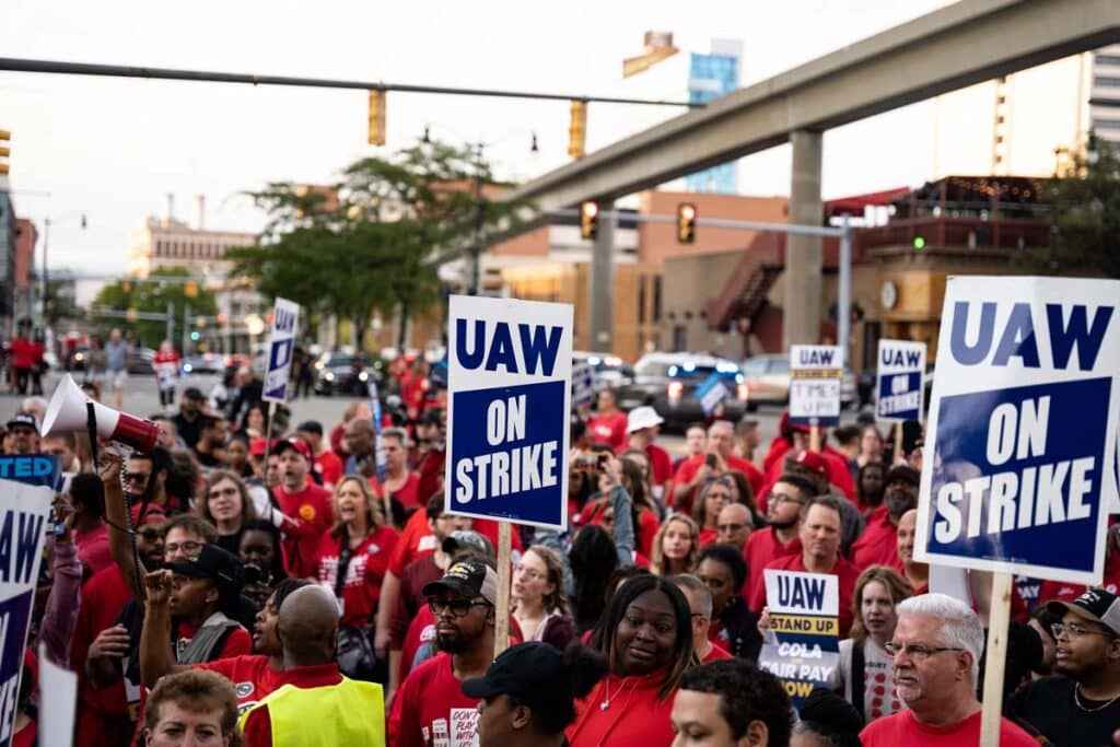 Protestors holding 'UAW on strike' signs, representing the UAW strike.