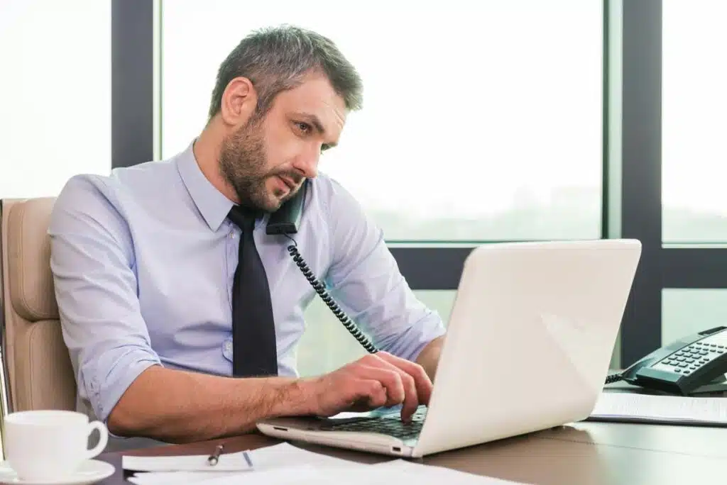 Businessman on the phone in an office while typing on a laptop, representing the Global Trade Hub settlement.