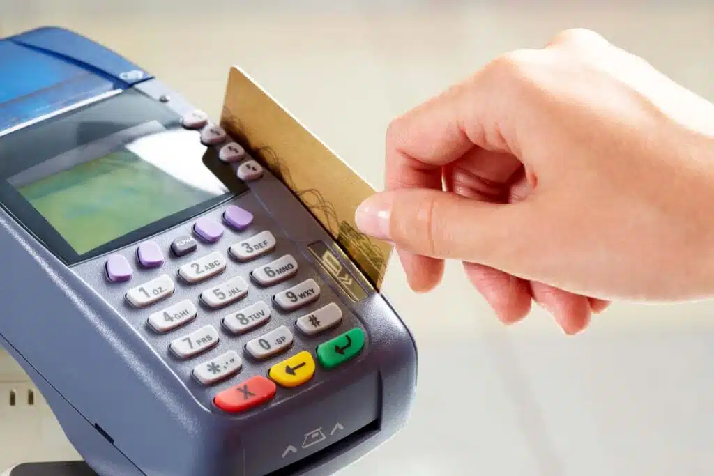 Close up of a woman's hand swiping a debit card on a POS machine, representing debit card swipe fees.
