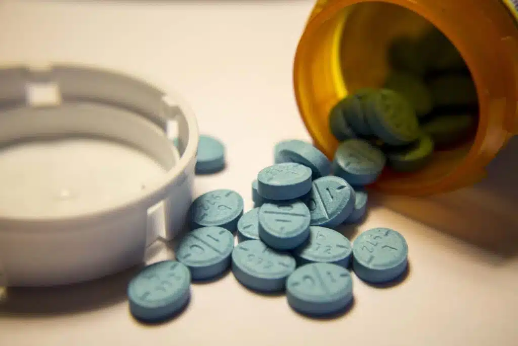 Close up of blue Adderall pills spilling out of a pill bottle, representing the Adderall shortage.