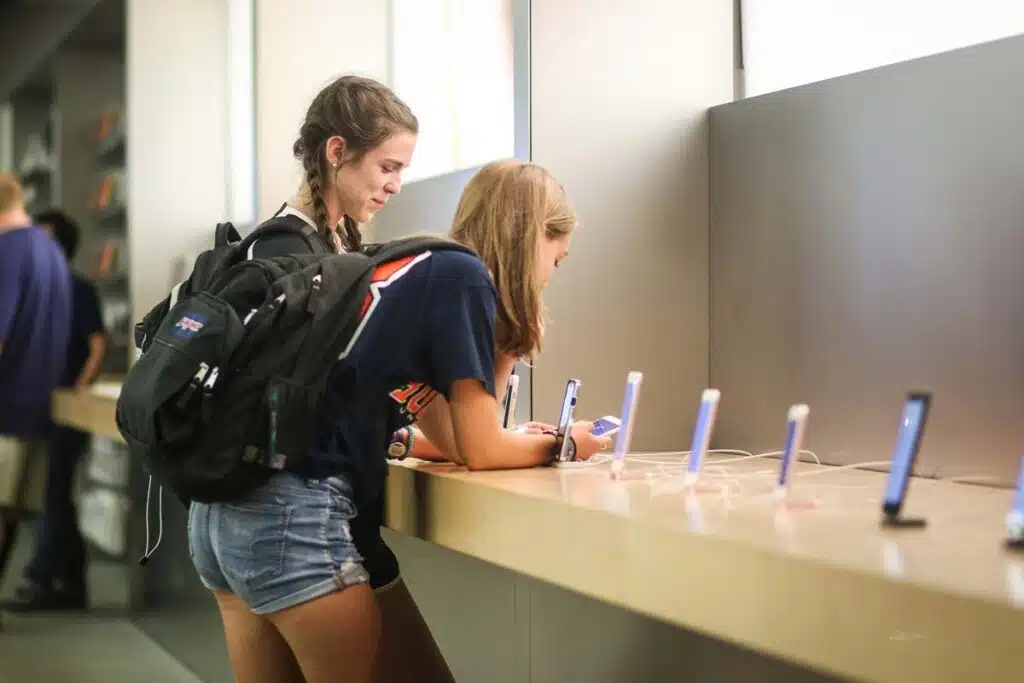 Two teen girls looking at new iPhones in an Apple Store, representing the teens iPhone report.