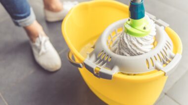 Close-up of a woman in white shoes and jeans wringing out a mop in a yellow bucket, representing the Pine-Sol settlement.