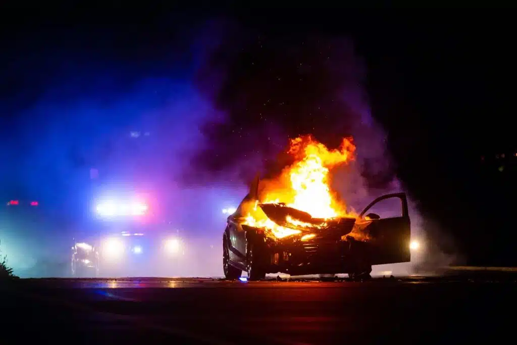 A car on fire with the police in the background, representing the NHTSA investigation into the Hyundai and Kia recalls.