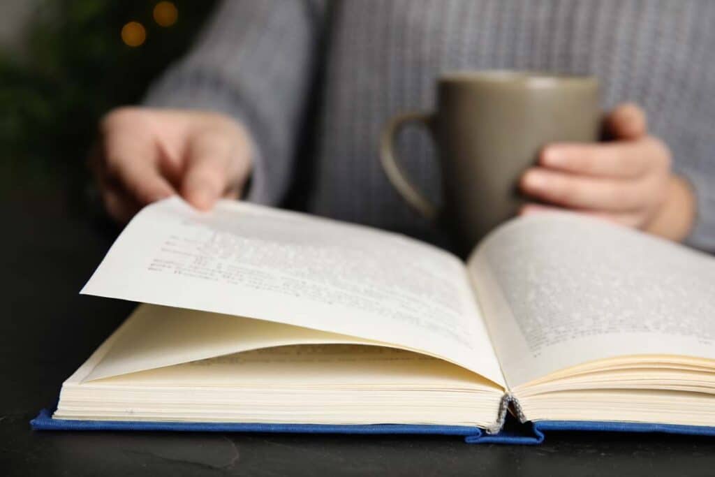 Close up of a woman holding a coffee mug and reading a book, representing physical books.