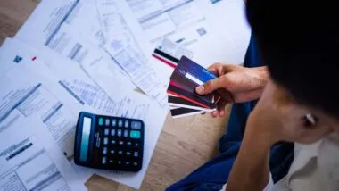 A woman looking down at her credit card bills while holding credit cards, representing credit card debt.