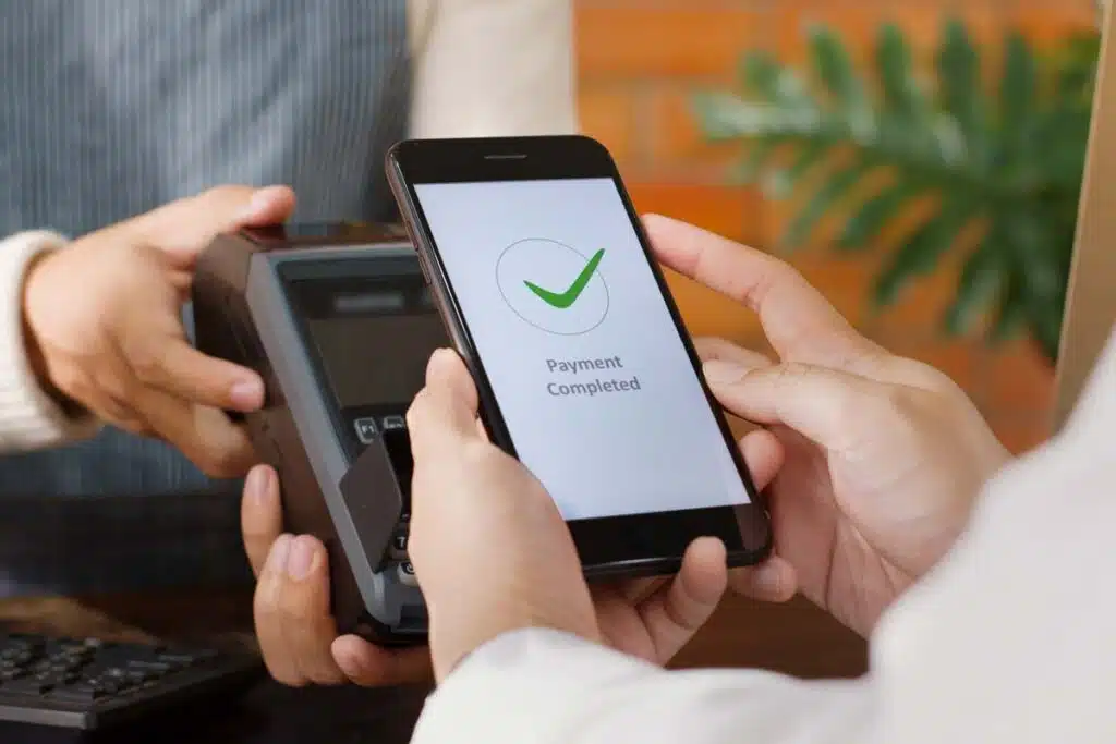 Close up of a customer using their smartphone to make a payment, representing digital wallets and payment apps.