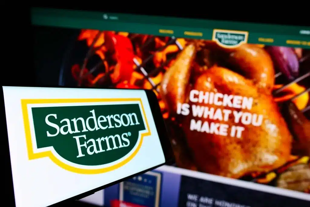 The Sanderson Farms logo is displayed on a smartphone screen with its website in the background, representing the Sanderson chicken prices verdict.
