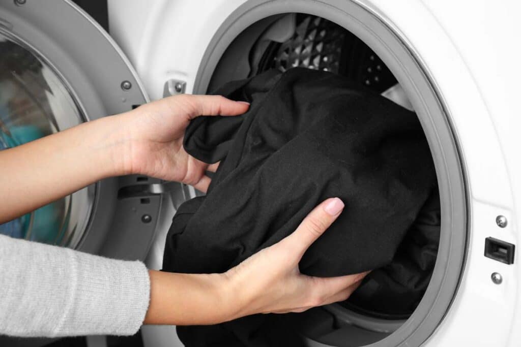 Close up of woman putting black clothes in a washer, representing the Woolite Color Renew class action lawsuit settlement.