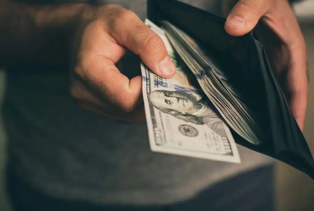 Close up of a man pulling cash out of his wallet, representing recent class action rebates.