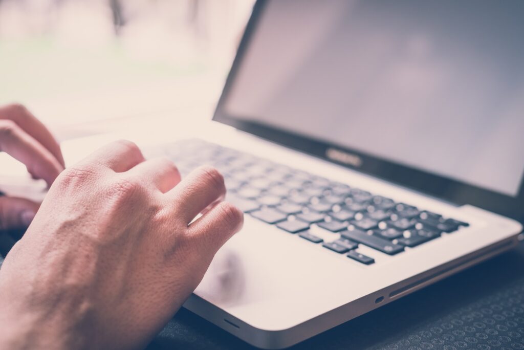 Closeup of a person's hands on the keyboard of a laptop, representing class action settlements closing soon.