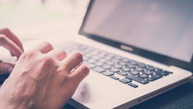 Closeup of a person's hands on the keyboard of a laptop, representing class action settlements closing soon.