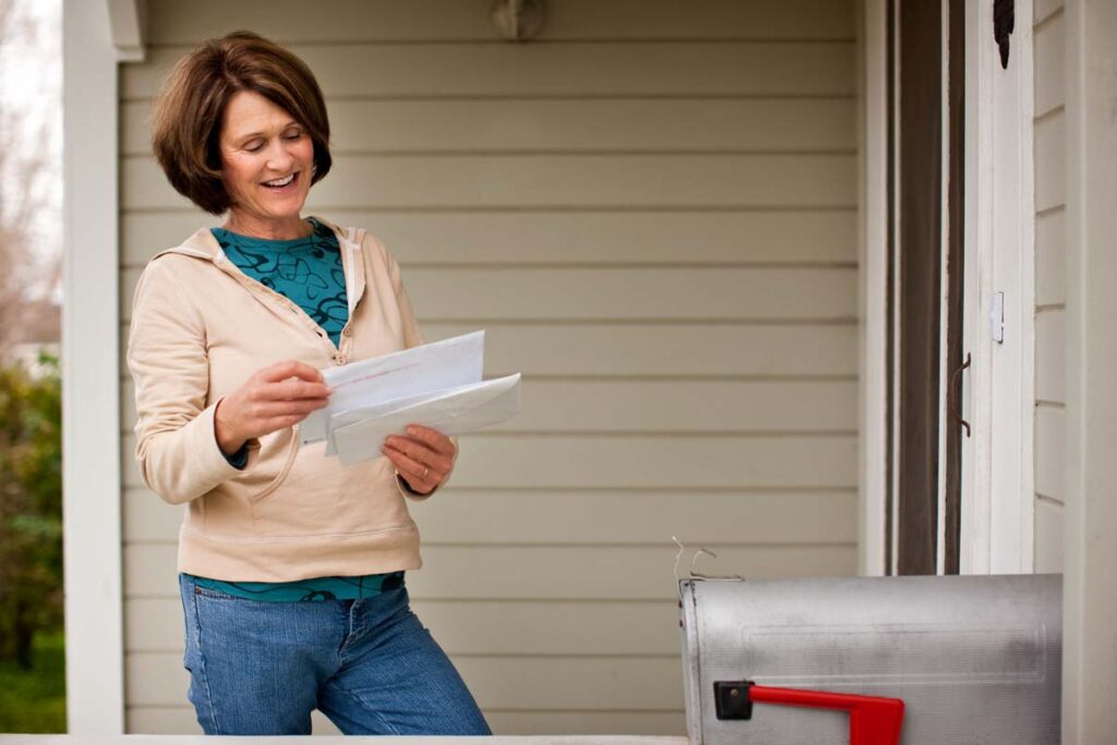 A happy woman reading mail after checking her mailbox, representing recent settlement checks in the mail.