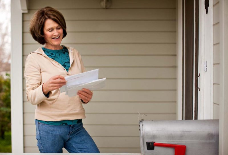 A happy woman reading mail after checking her mailbox, representing recent settlement checks in the mail.