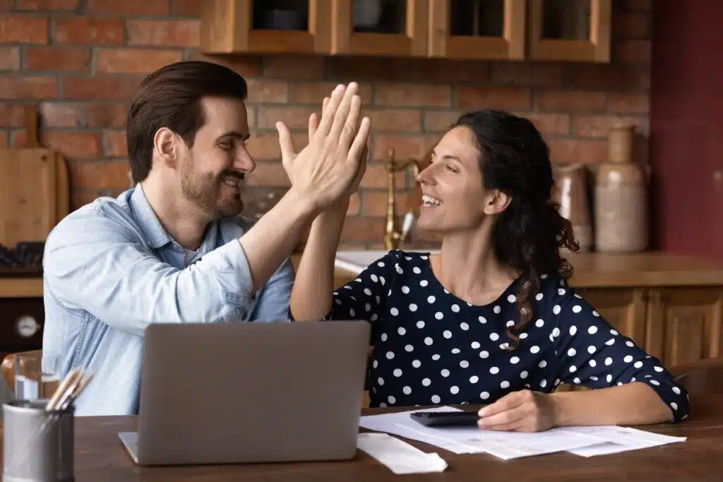 A couple high-fives behind a laptop and table full of papers, representing settlements closing soon.